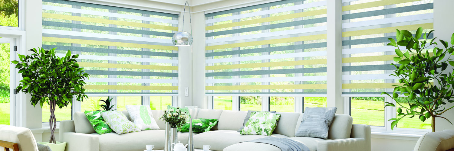 Bright conservatory with large windows fitted with grey motorised blinds, white corner sofa and indoor plants