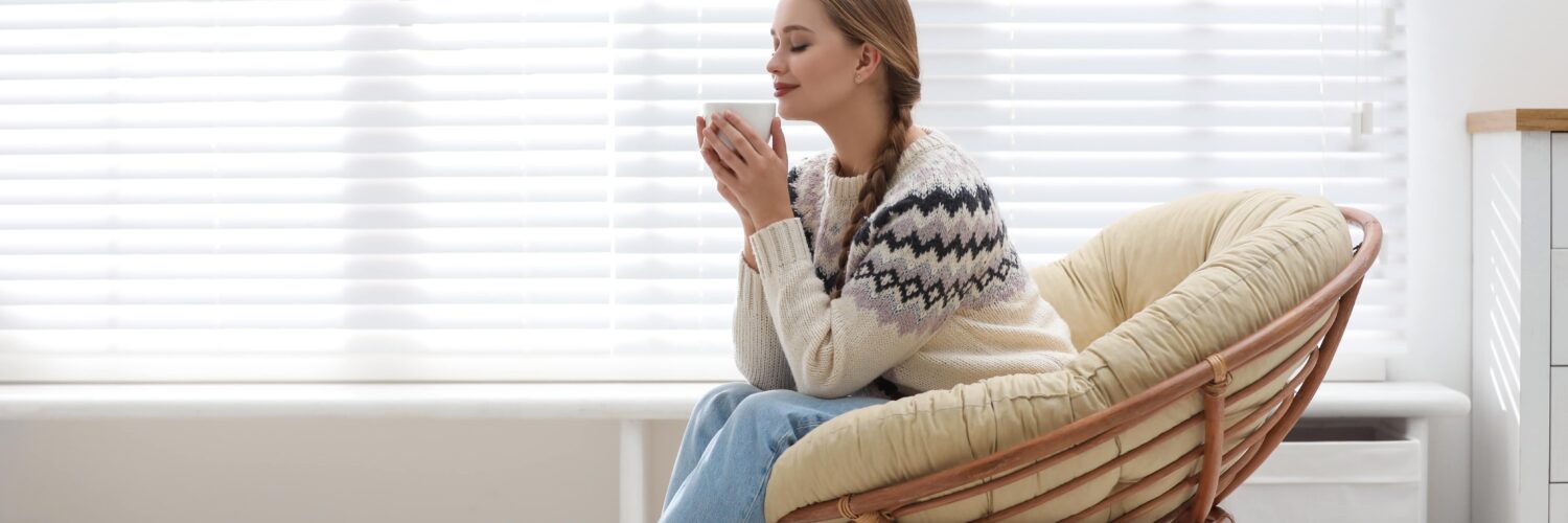 woman-on-chair-drinking-in-warmth-next-to-blinds