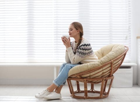 woman-on-chair-drinking-in-warmth-next-to-blinds