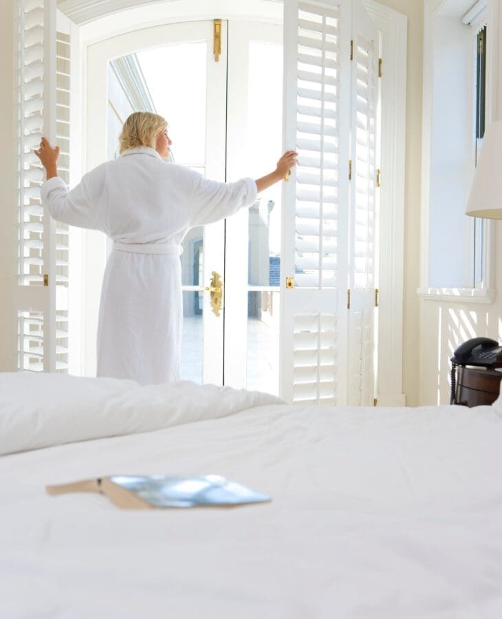 woman-opening-full-height-shutters-in-bedroom