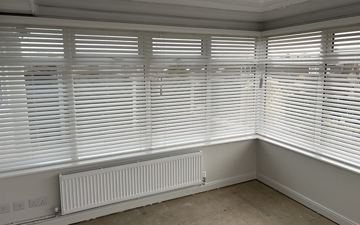 White made to measure conservatory blinds installed on large corner windows in a modern UK home.