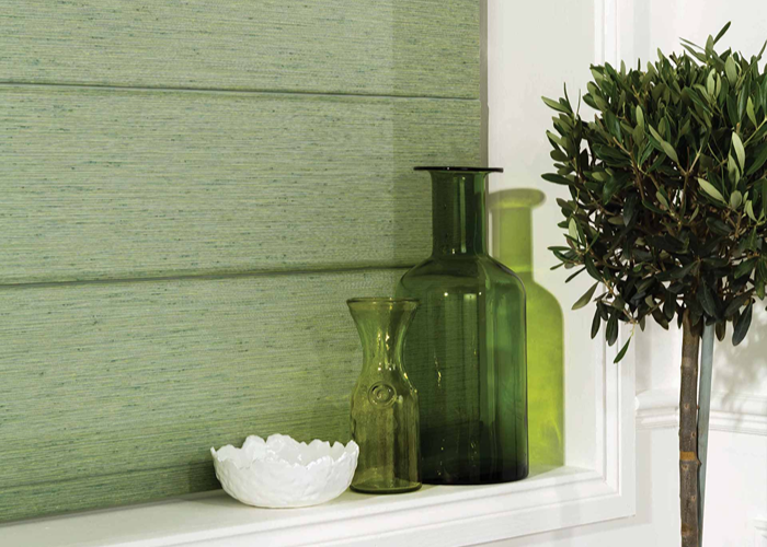 Green textured bathroom Roman blind with decorative glassware and indoor plant on a windowsill.