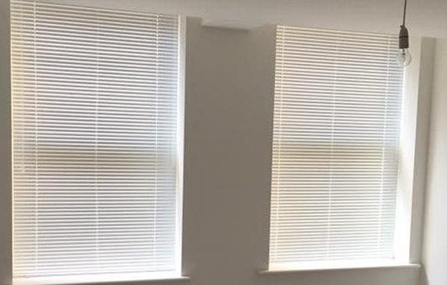 White Venetian blinds partially closed on two bathroom windows in a minimalist space.