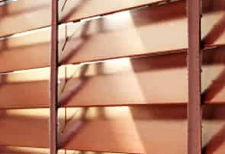 Close-up of wooden bathroom blinds with warm-toned slats filtering natural light.